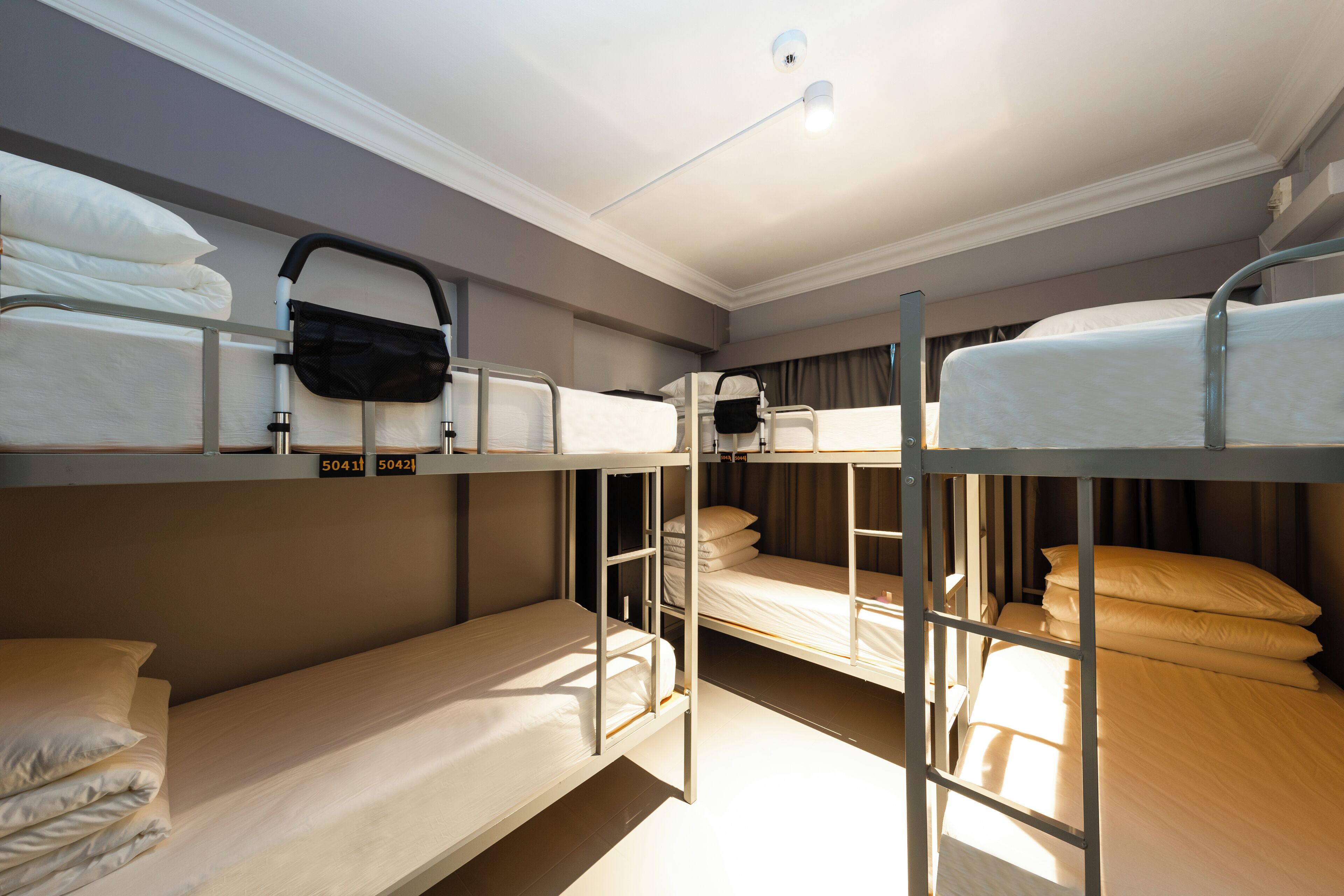 A bunk bed room with three beds, each with a pillow and a bag.