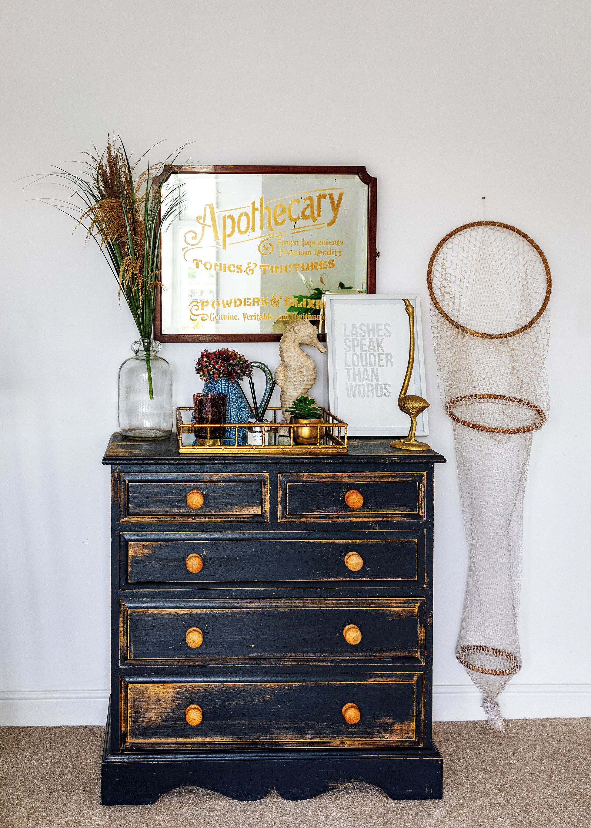 A dark wooden dresser with gold knobs, a framed sign above it, and a decorative net hanging on the wall.