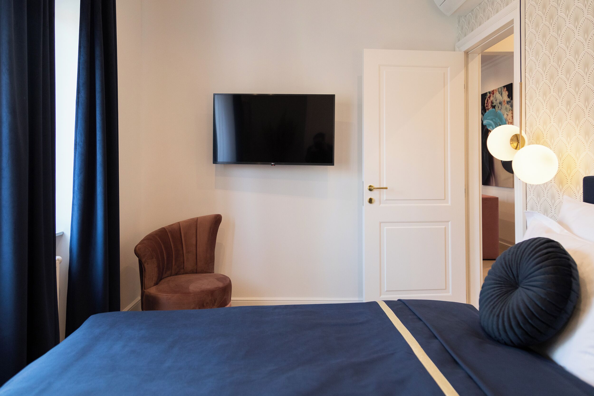 A hotel room with a bed, a TV mounted on the wall, a brown armchair, and a door leading to a bathroom.
