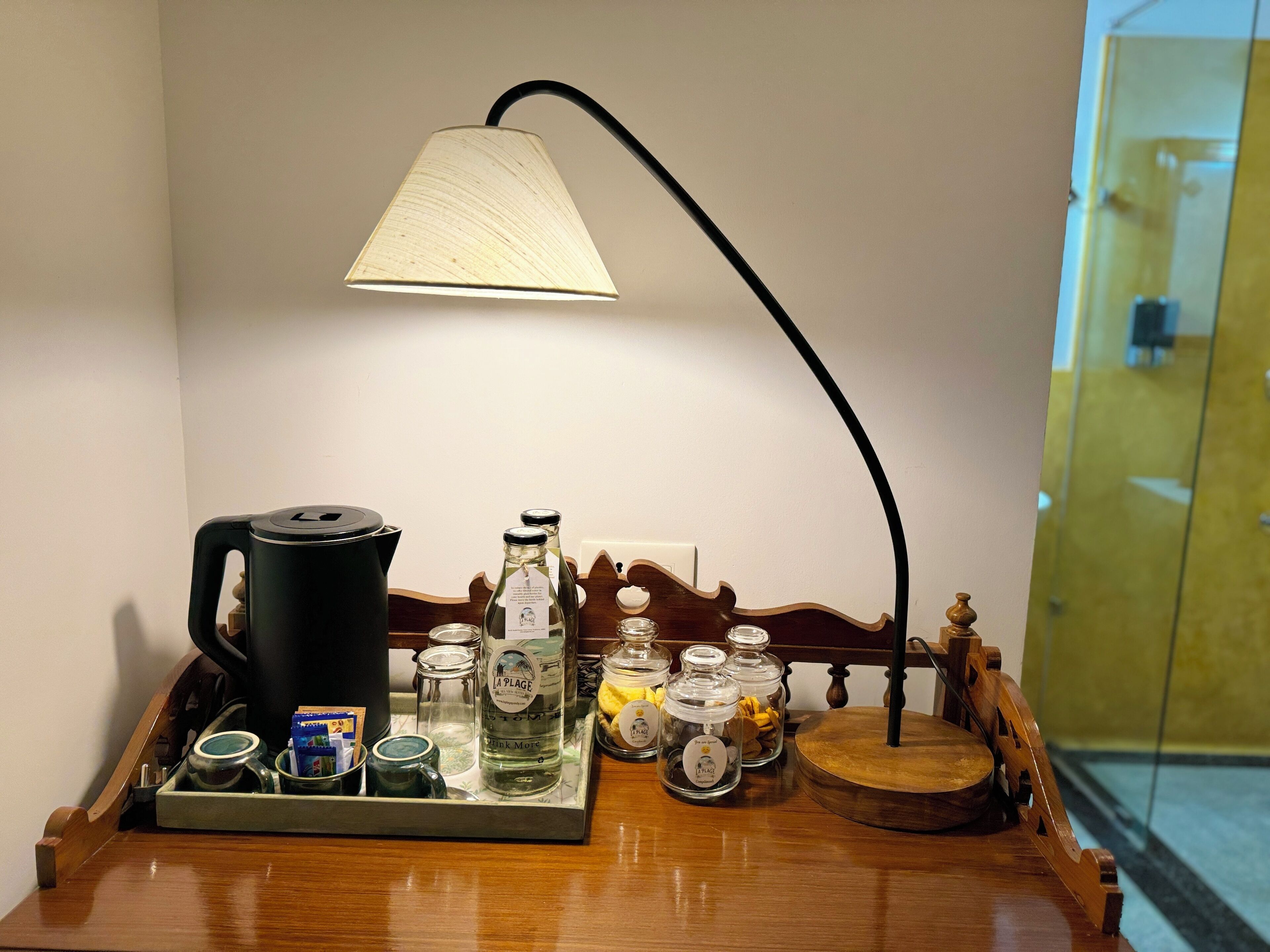 A wooden tray with a coffee maker, a bottle of water, and several glass jars on a table.