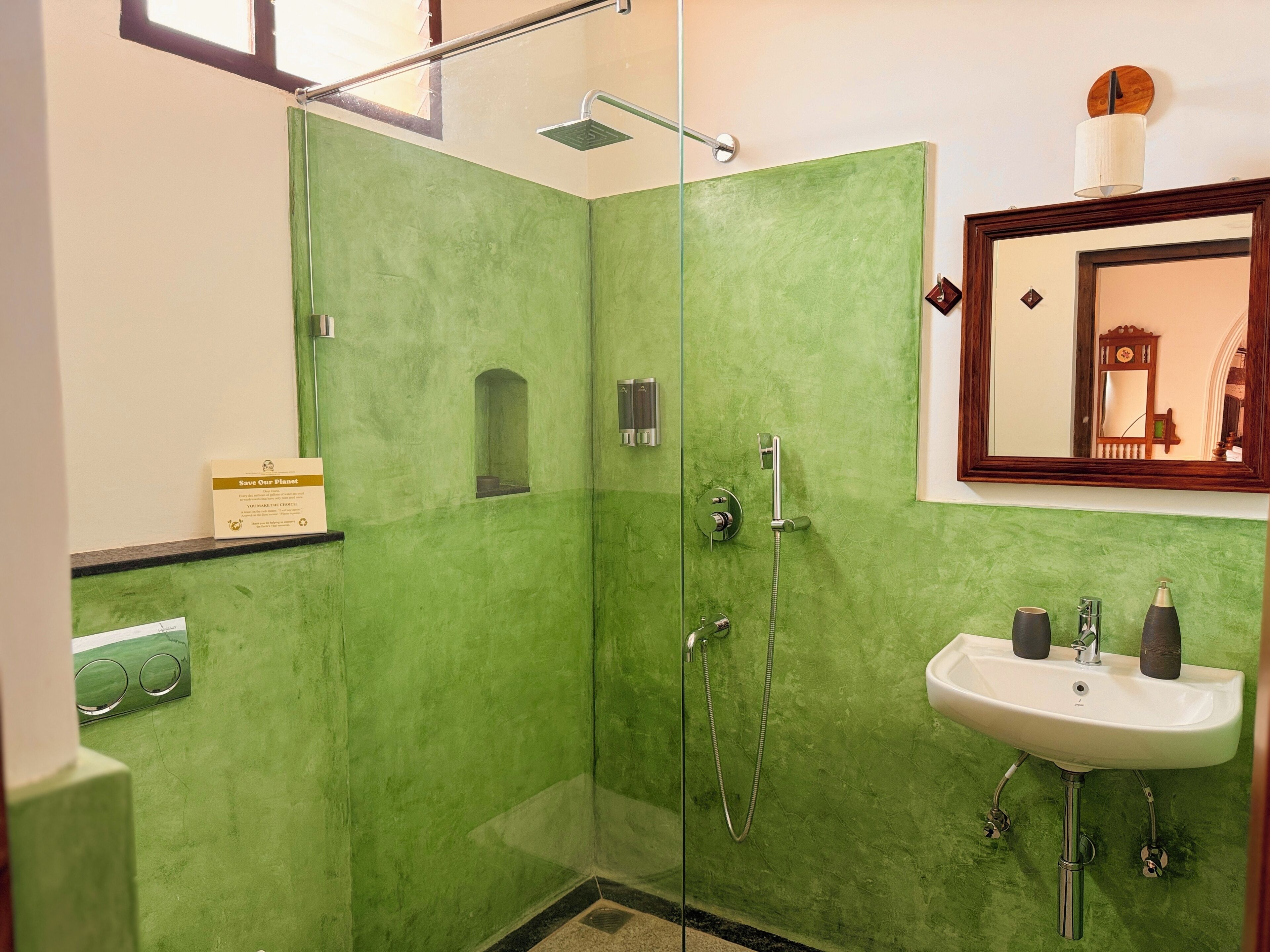 A bathroom with green walls, a glass shower enclosure, a sink with two bottles, and a mirror above the sink.