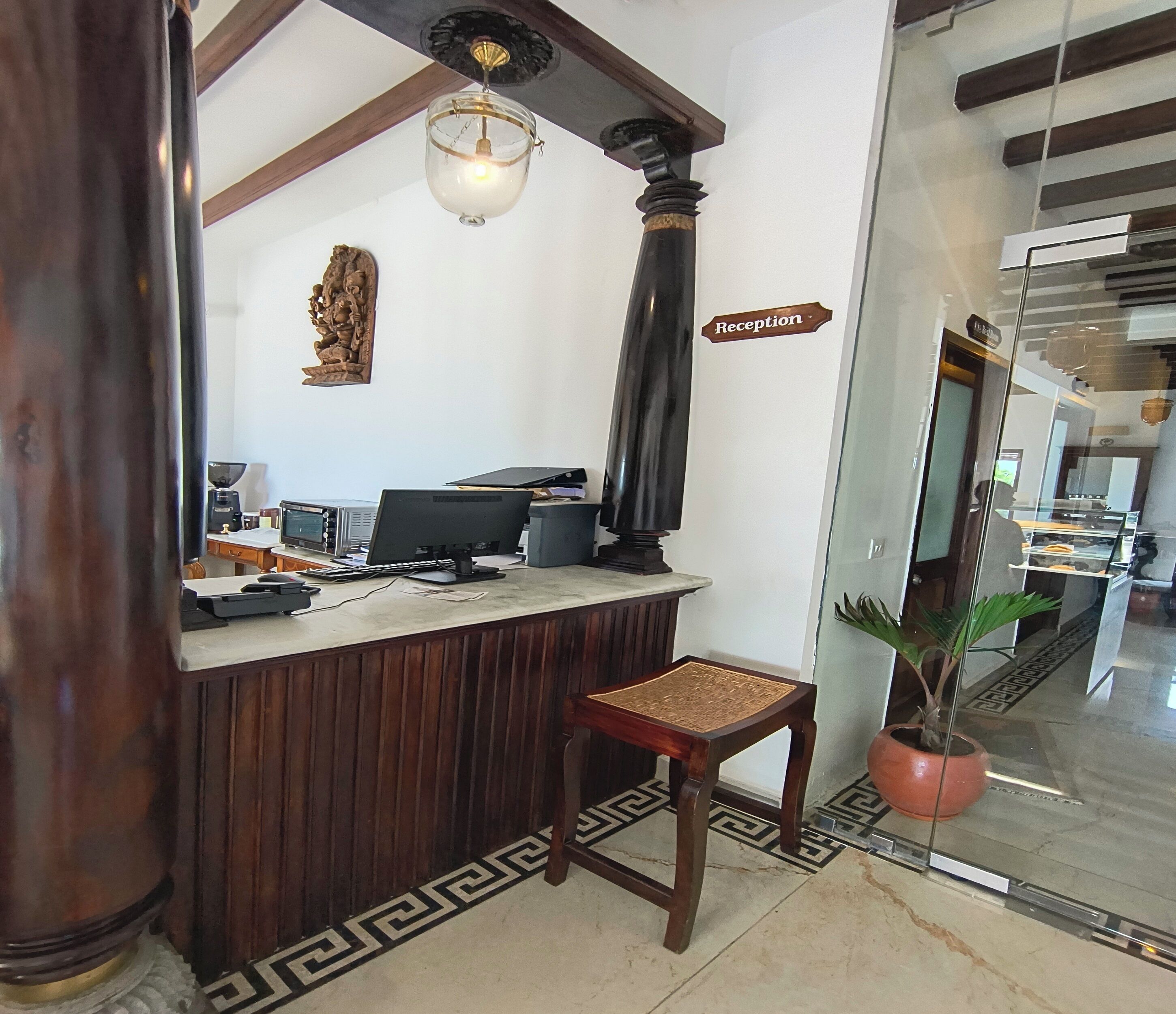 A reception desk with a computer, a telephone, and a small chair. There is a reception sign on the wall and a potted plant near the entrance.