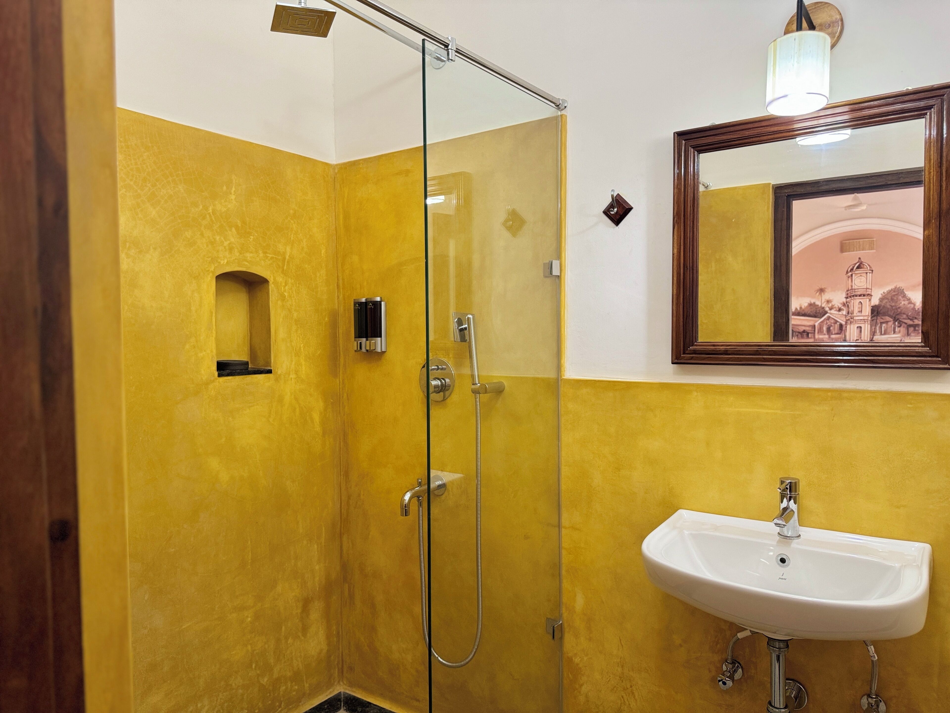 A bathroom with a glass-enclosed shower, a white sink, and a mirror with a picture frame.