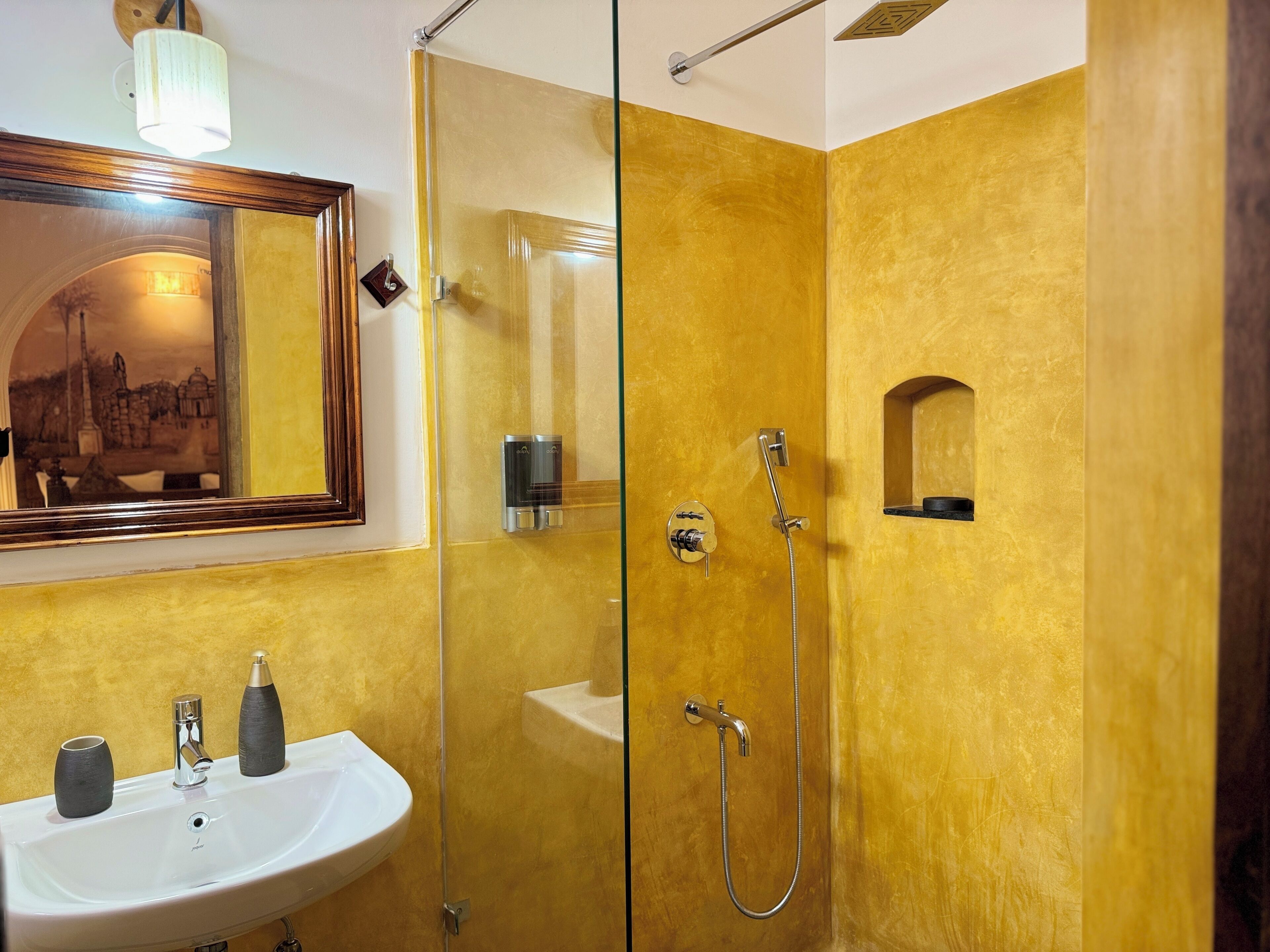 Une salle de bain avec un lavabo blanc, un miroir et une douche dotée d’une porte en verre.