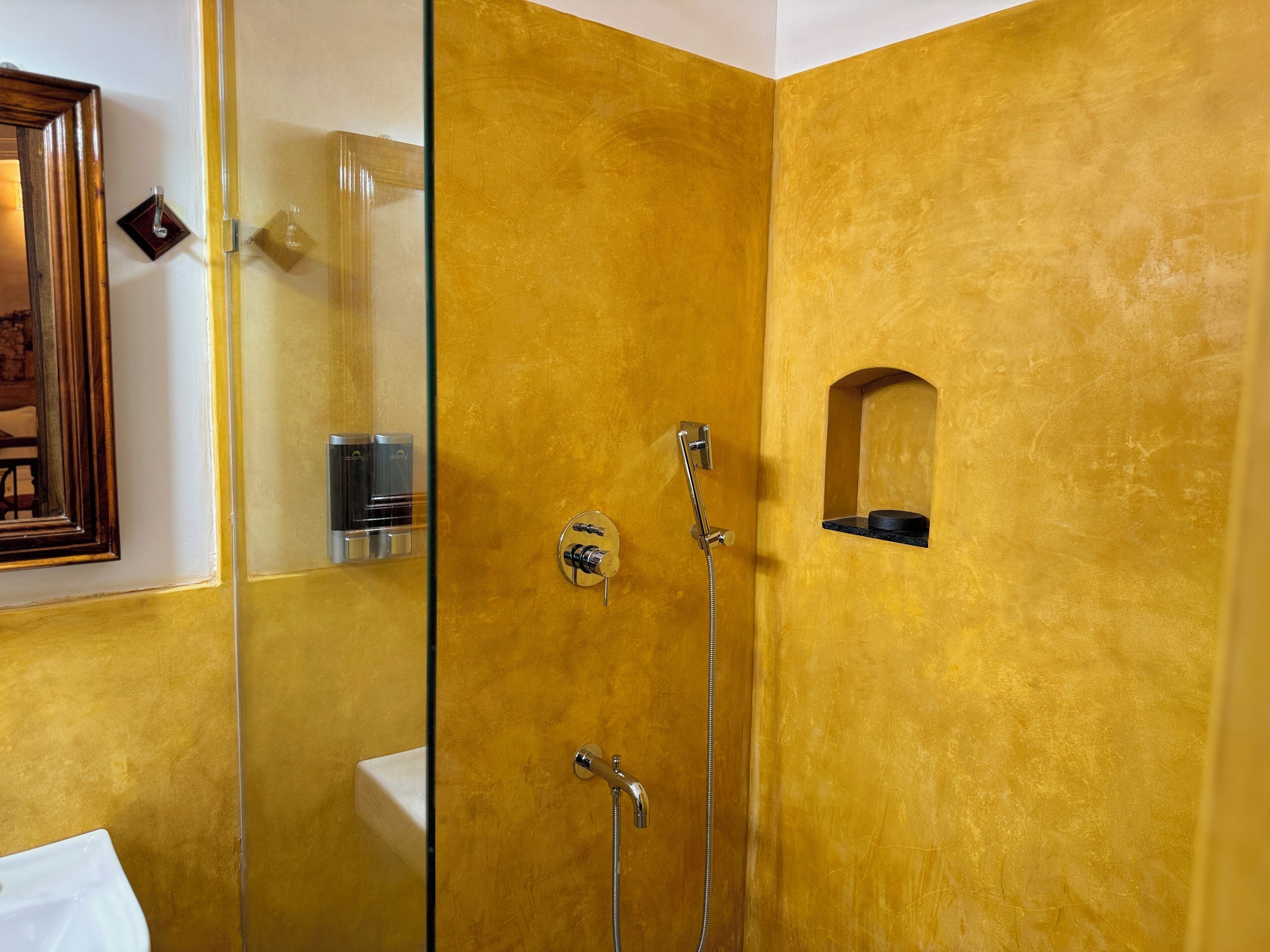 A bathroom with a yellow textured wall, a glass shower enclosure, a sink, and a small shelf with toiletries.