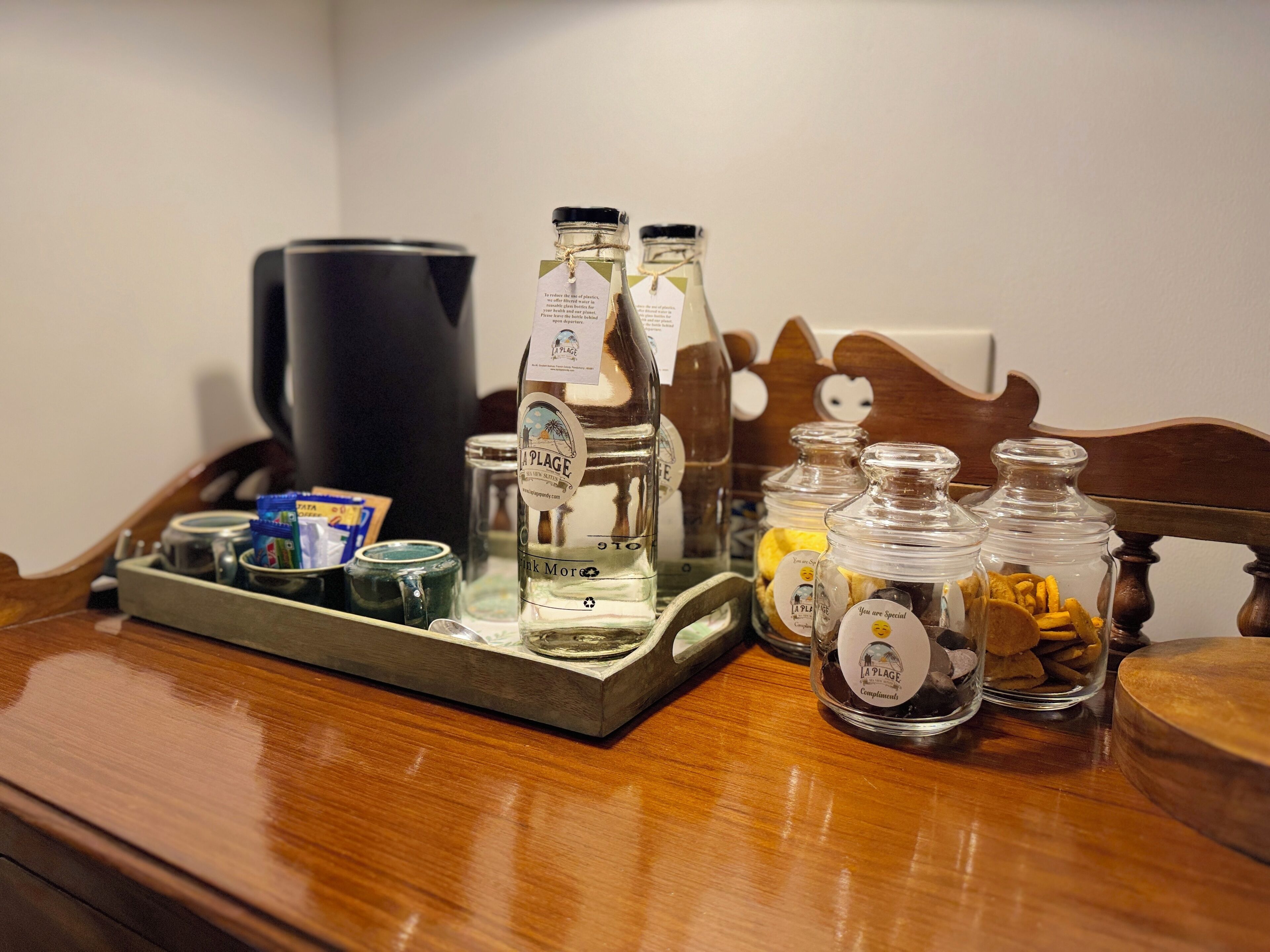 A wooden table with a tray holding a bottle of water, a coffee maker, and jars labeled "La Plage".