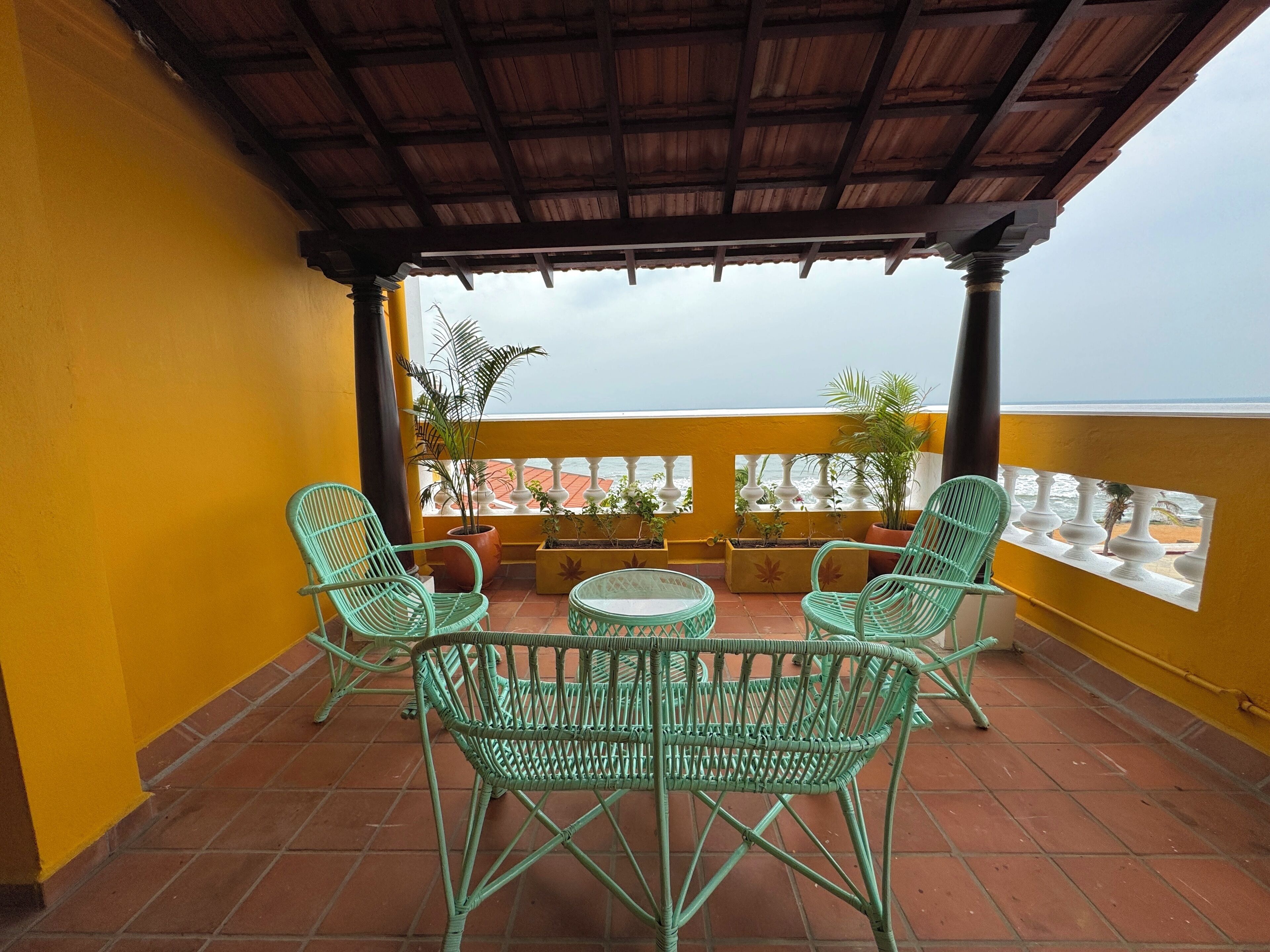 A terrace with green wicker furniture, a small round table, and potted plants.