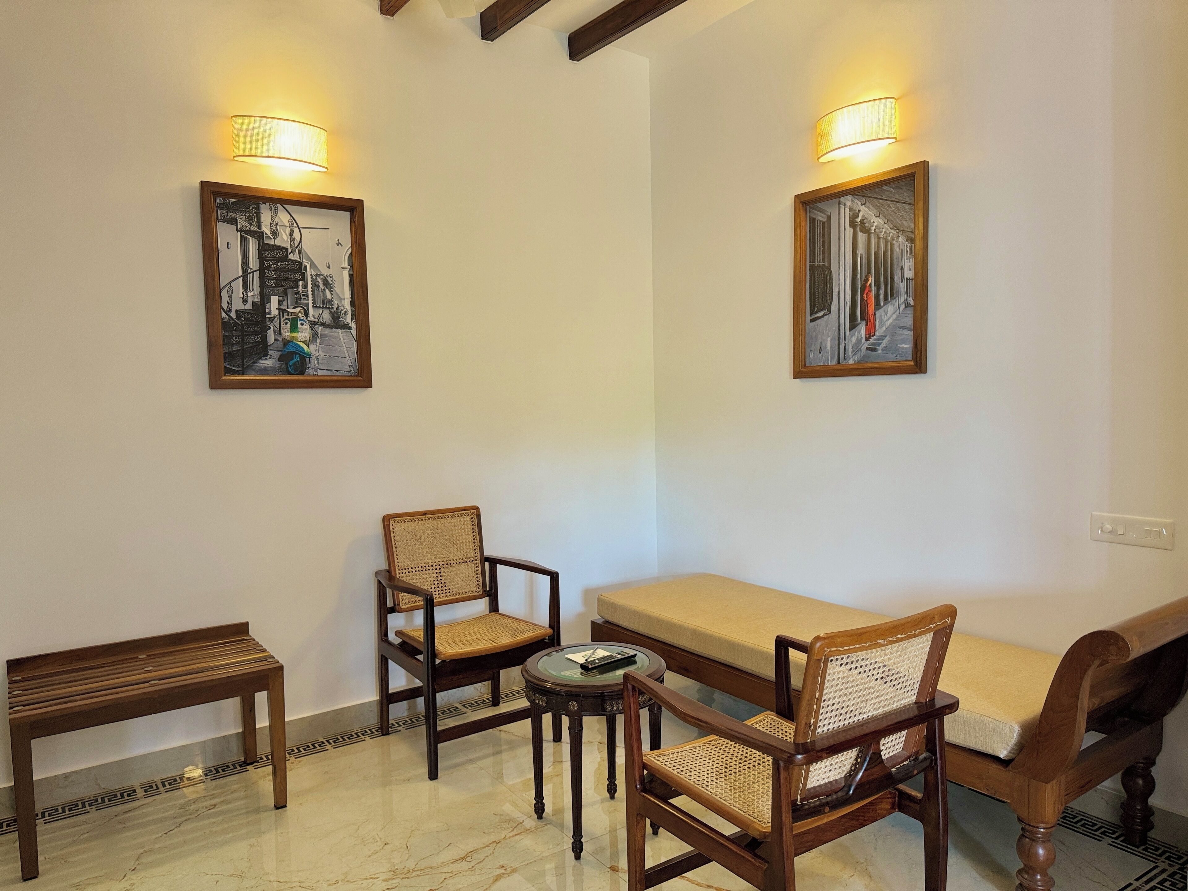 A room with a sofa, two wooden chairs, a small round table, and two wall-mounted lamps.
