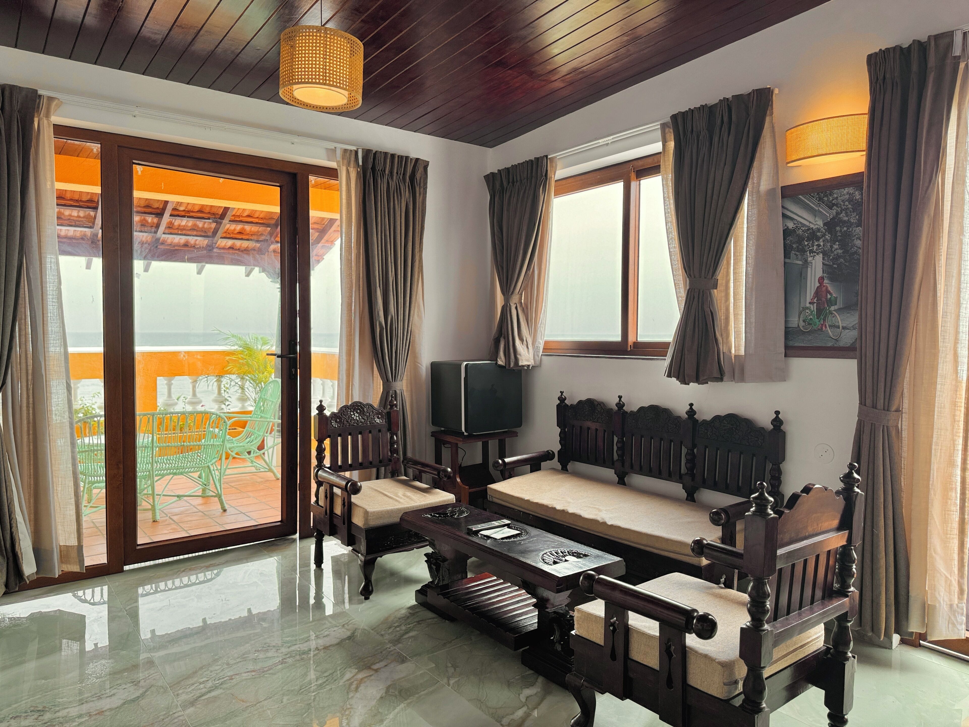 A room with a wooden ceiling, a sofa, a television, and a view of the outside balcony.