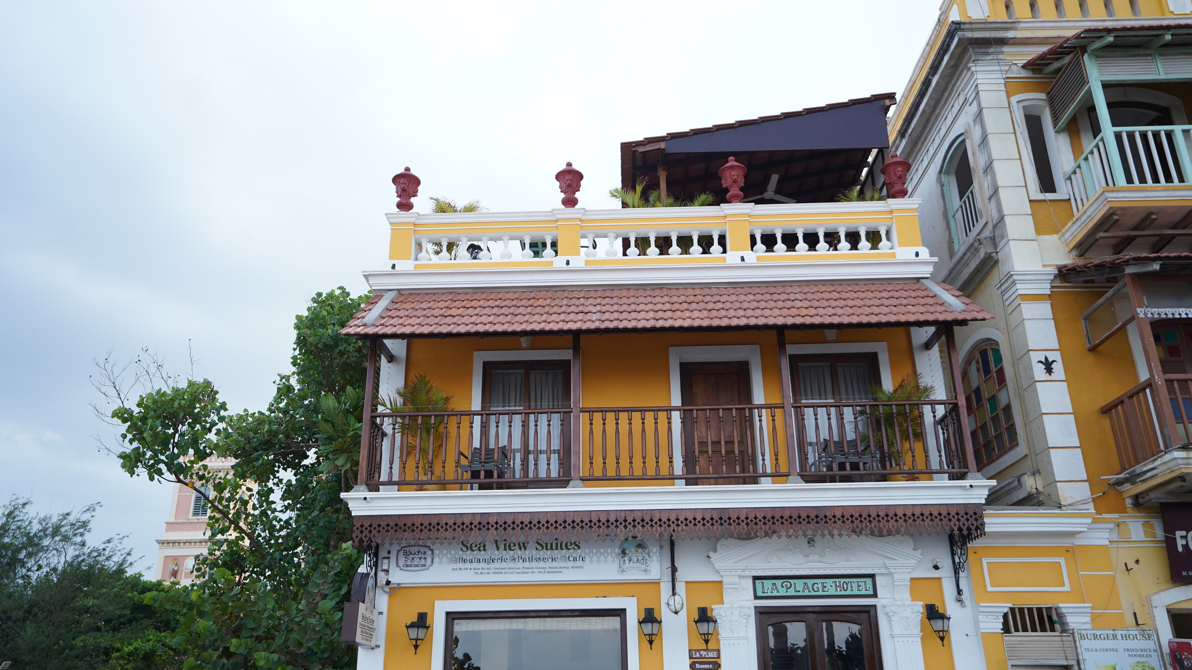 A multi-story hotel with a yellow facade, balconies with wooden railings, and a sign for 'La Plage Hotel'.