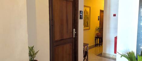 A hallway with a wooden door, a potted plant, and a tiled floor.