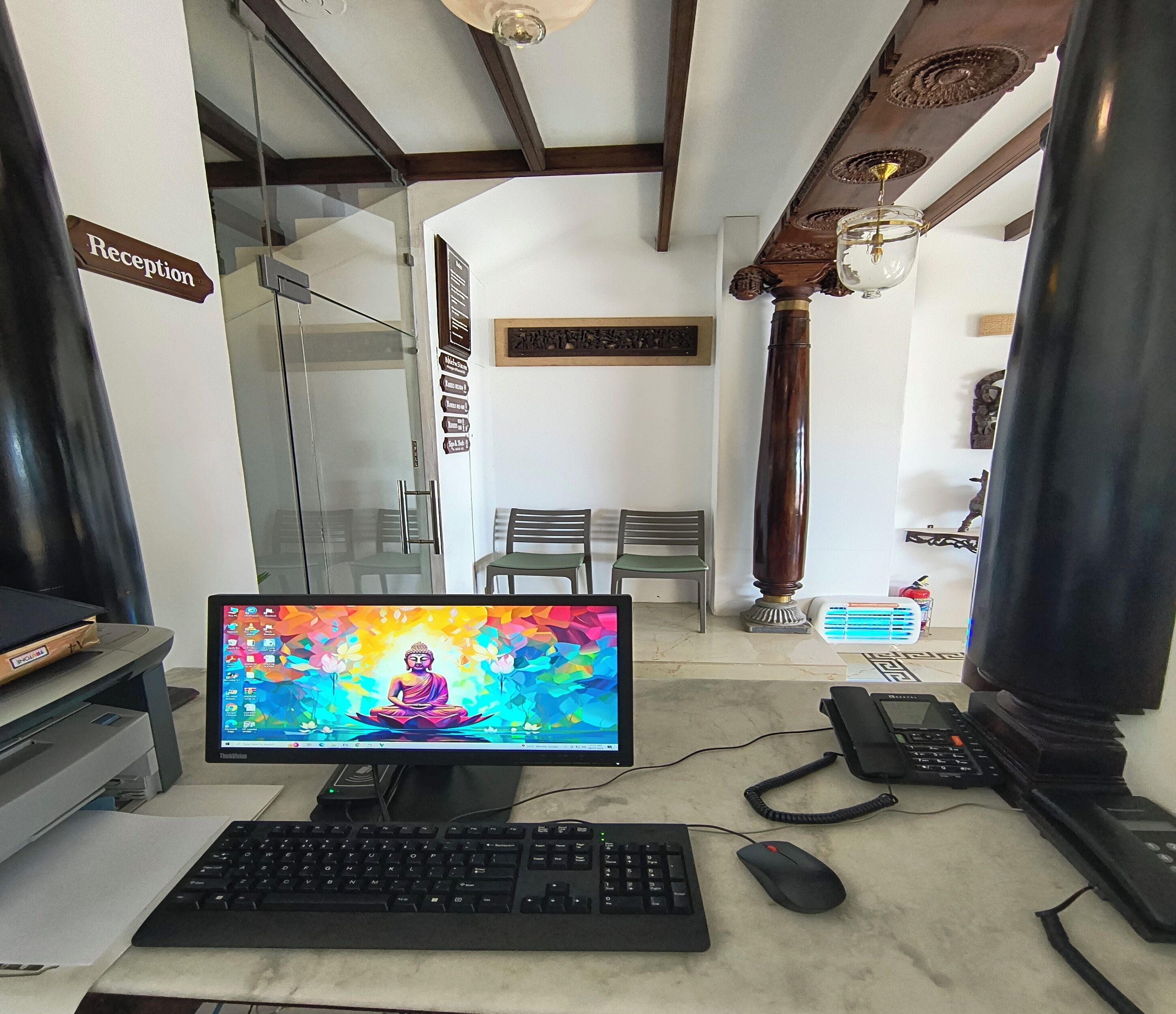 A reception desk with a computer monitor displaying a colorful Buddha image, a keyboard, a mouse, and a telephone.