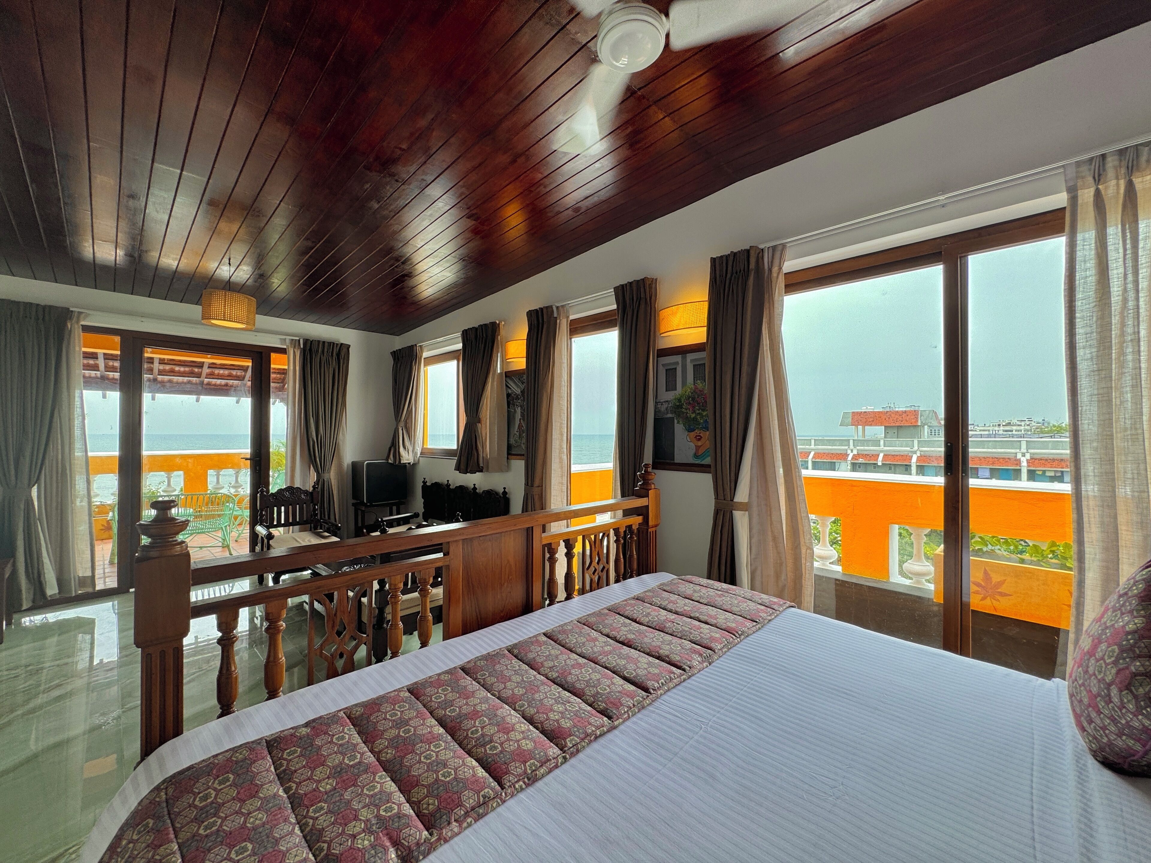 Habitación de hotel con una cama grande, techo de madera y un balcón con vistas a la ciudad.