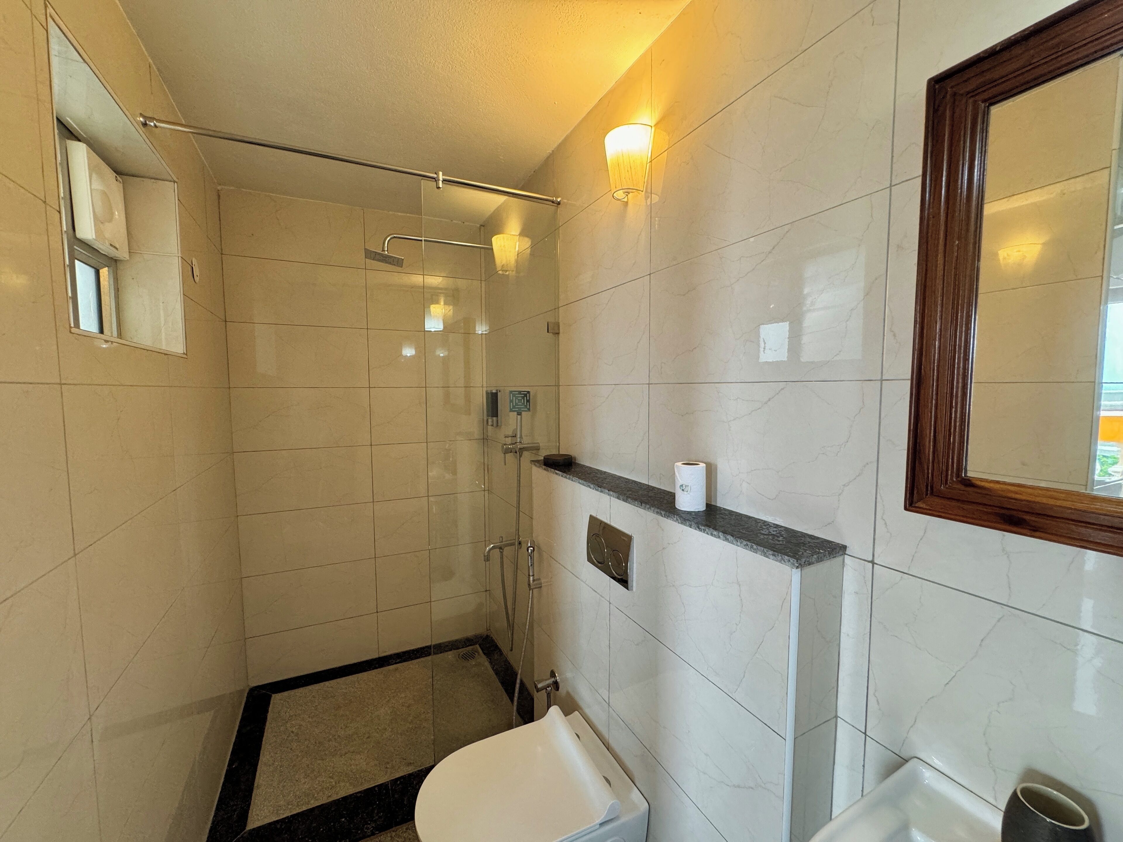 Een badkamer met een douchecabine van glas, een toilet, een wastafel en een spiegel.