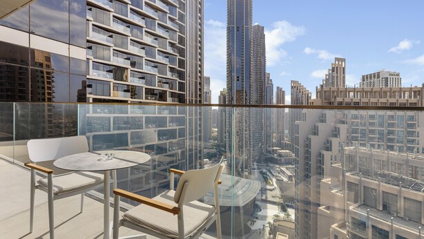 A high-rise building with a glass balcony, furnished with two chairs and a small round table, offering a city view. - Maison Privee - Elegant Coastal Apt on Palm Jumeirah (Dubai)