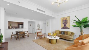 A modern living room with a sofa, a coffee table, and a dining area with a table and chairs. - Maison Privee - Elegant Coastal Apt on Palm Jumeirah (Dubai)