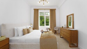 A modern bedroom with a large bed, a wooden dresser, a bedside table, a mirror, and a window with curtains. - Maison Privee - Elegant Coastal Apt on Palm Jumeirah (Dubai)