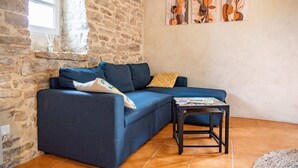 En stue med en stenvæg, en blå sofa, et lille bord og abstrakt vægkunst.
