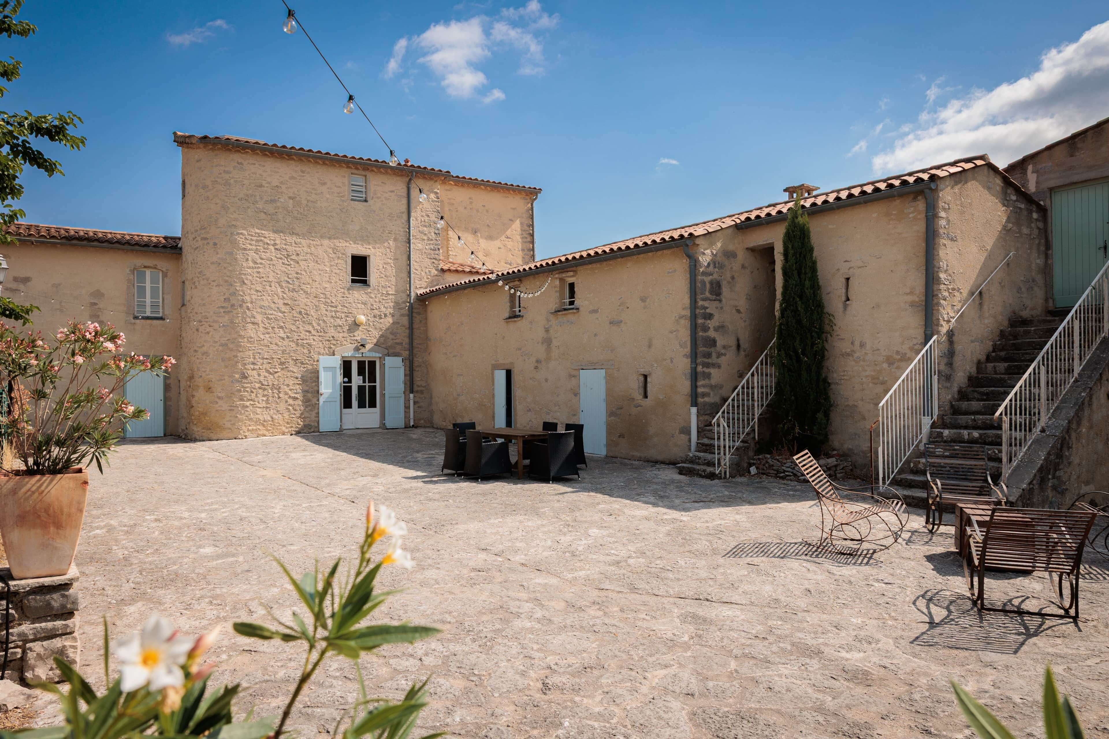 A courtyard with a stone floor, a staircase, and a dining area with outdoor furniture.