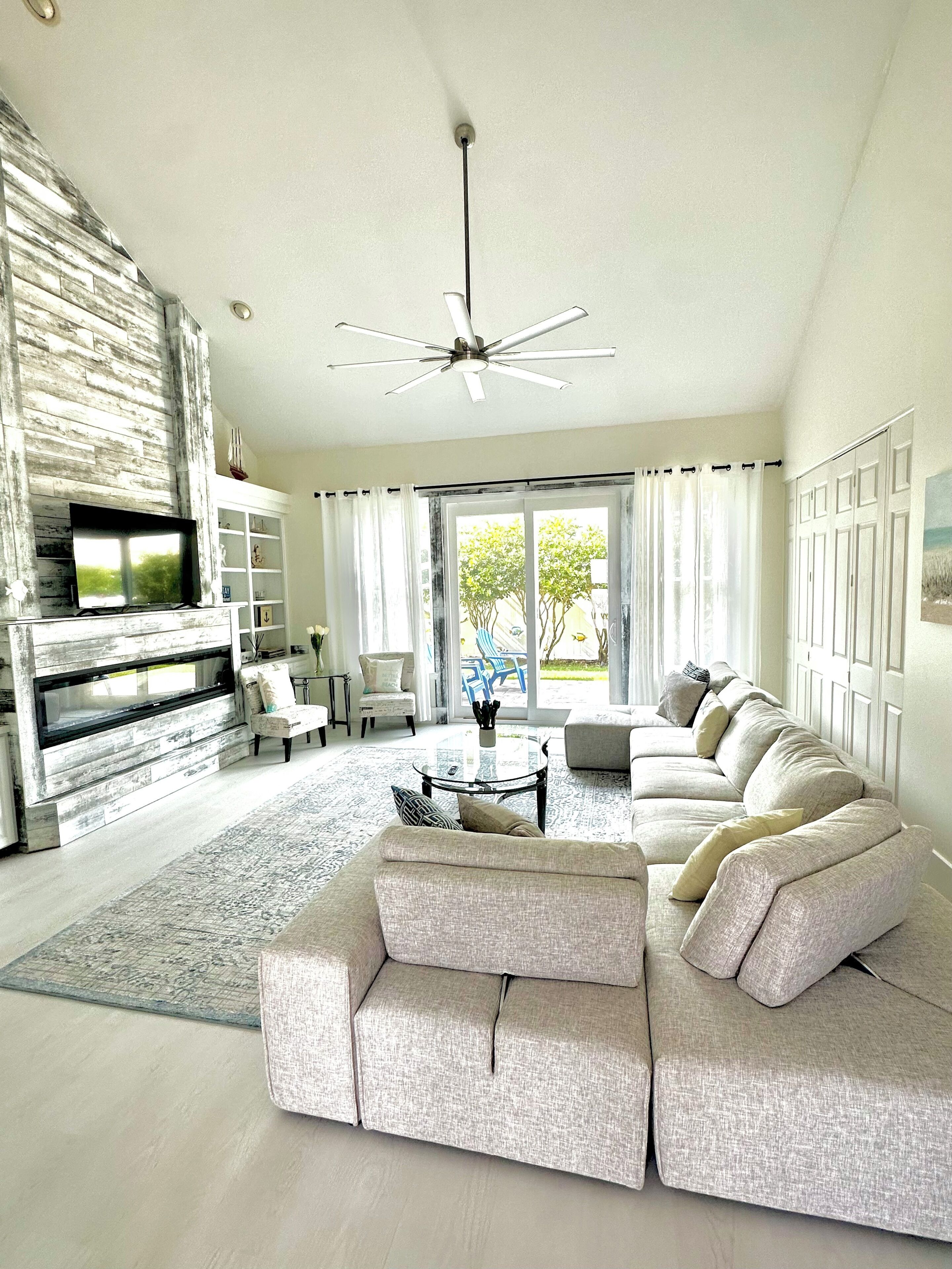 A modern living room with a sectional sofa, a flat-screen TV, a fireplace, and a ceiling fan.
