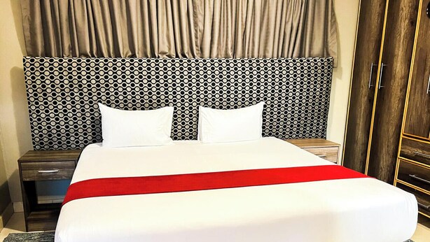 Una habitación de hotel con una cama grande, un cabecero con diseño circular, una colcha roja y una mesita de noche de madera.