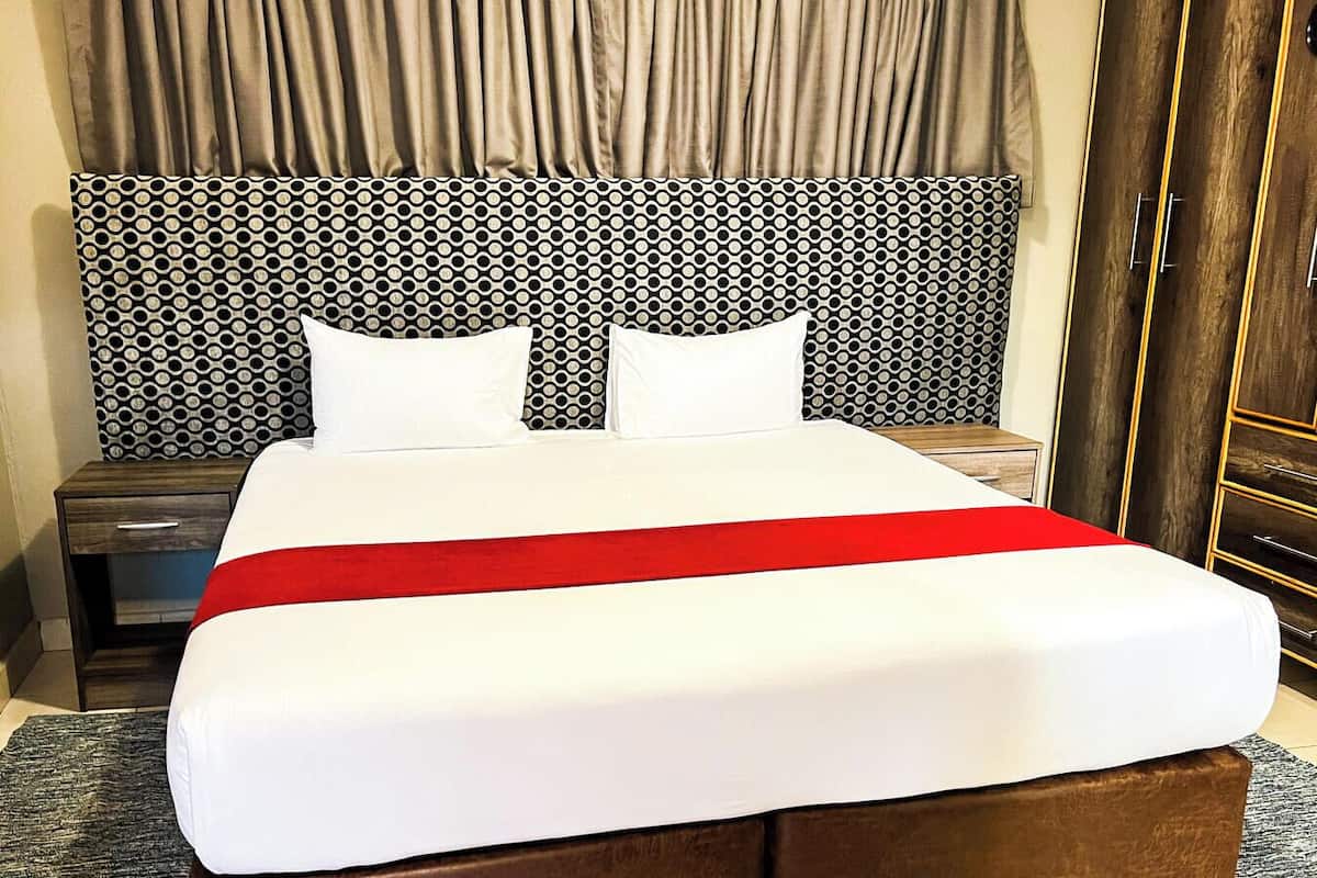 Una habitación de hotel con una cama grande, un cabecero con diseño circular, una colcha roja y una mesita de noche de madera.