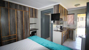 Una habitación de hotel compacta con cama, escritorio, kitchenette y baño.