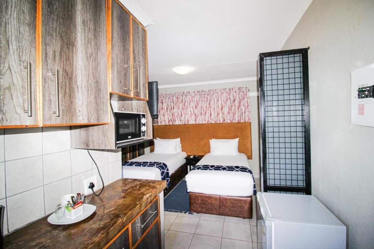 Una habitación de hotel compacta con kitchenette, dos camas, un microondas y un refrigerador pequeño.