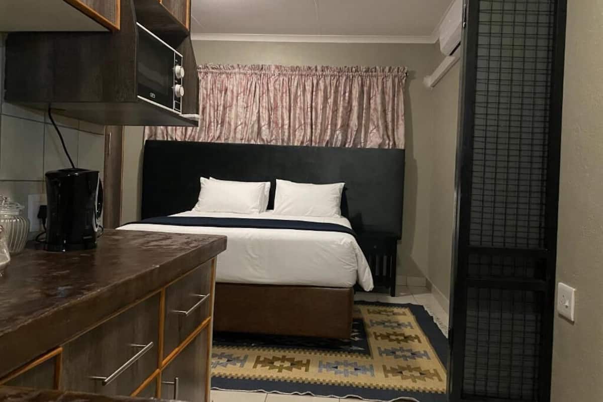Un dormitorio con una cama, un aparador de madera, una cafetera y una alfombra estampada.