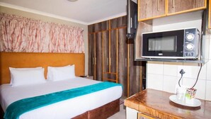 Una habitación de hotel con una cama, kitchenette con microondas y un televisor montado en la pared.