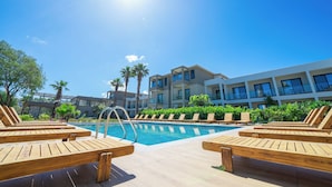 A pool area with wooden loungers, a clear blue sky, and modern buildings in the background. - Mare Alba (Bodrum)
