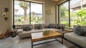 A modern living room with a sofa set, a wooden coffee table, and large windows offering a view of greenery and buildings. - Mare Alba (Bodrum)