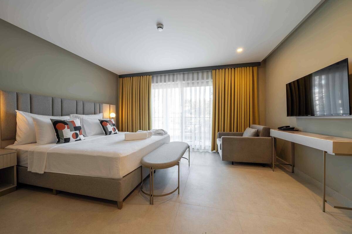 A modern hotel room with a large bed, a desk, a chair, and a TV.