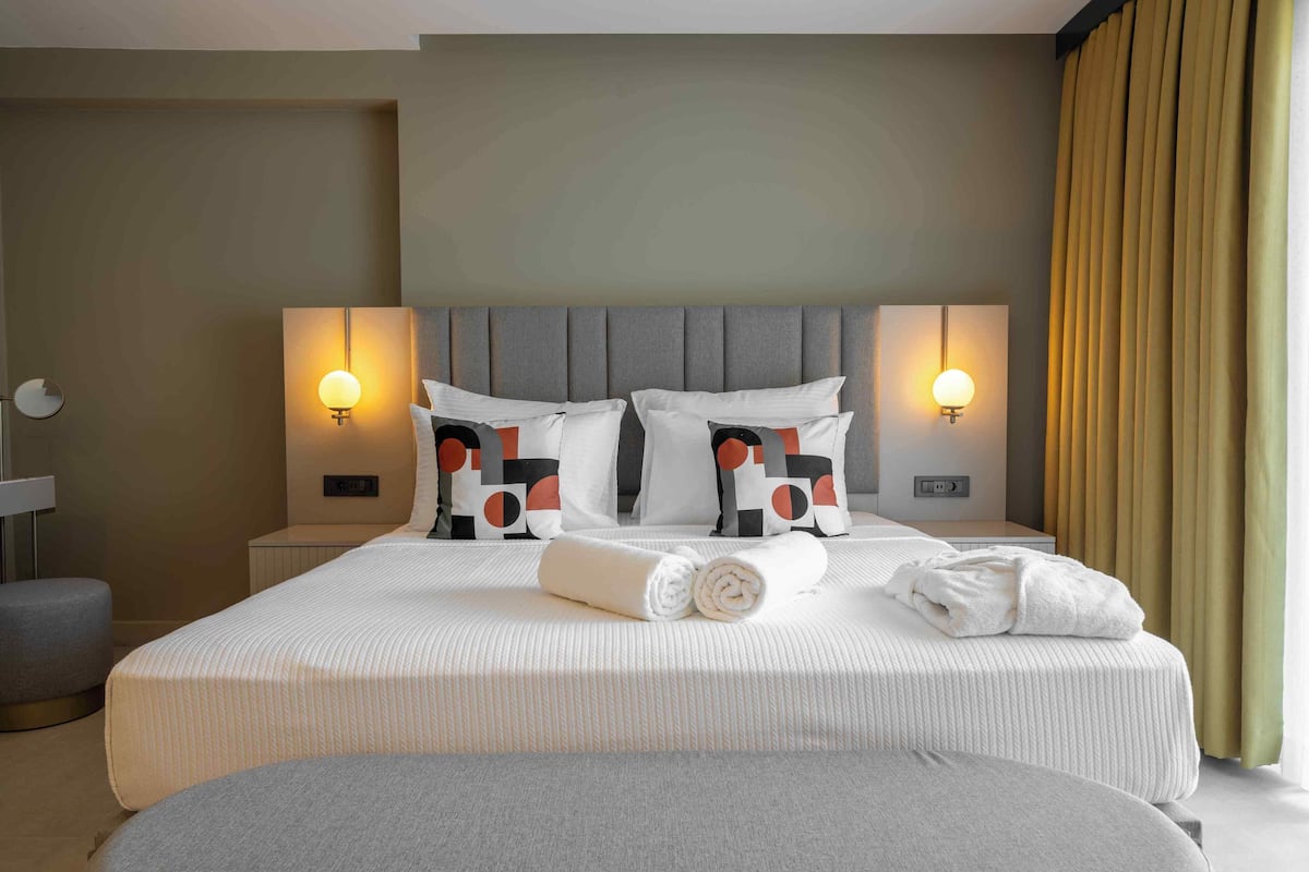 A hotel room with a large bed, two bedside lamps, a headboard, and a window with curtains.