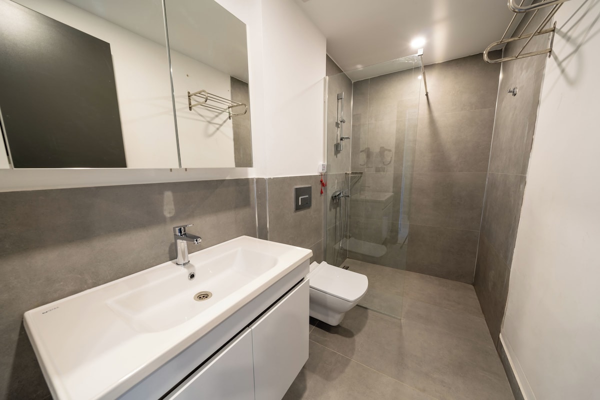 Ein modernes Badezimmer mit einem weißen Waschbecken, einer Toilette und einer Duschkabine aus Glas.