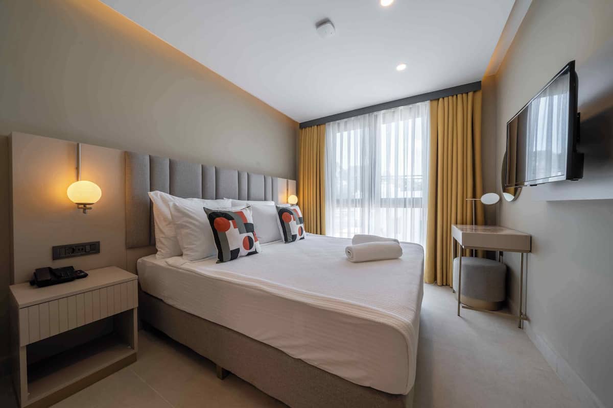 A modern hotel room with a large bed, bedside table, lamp, and a TV mounted on the wall.
