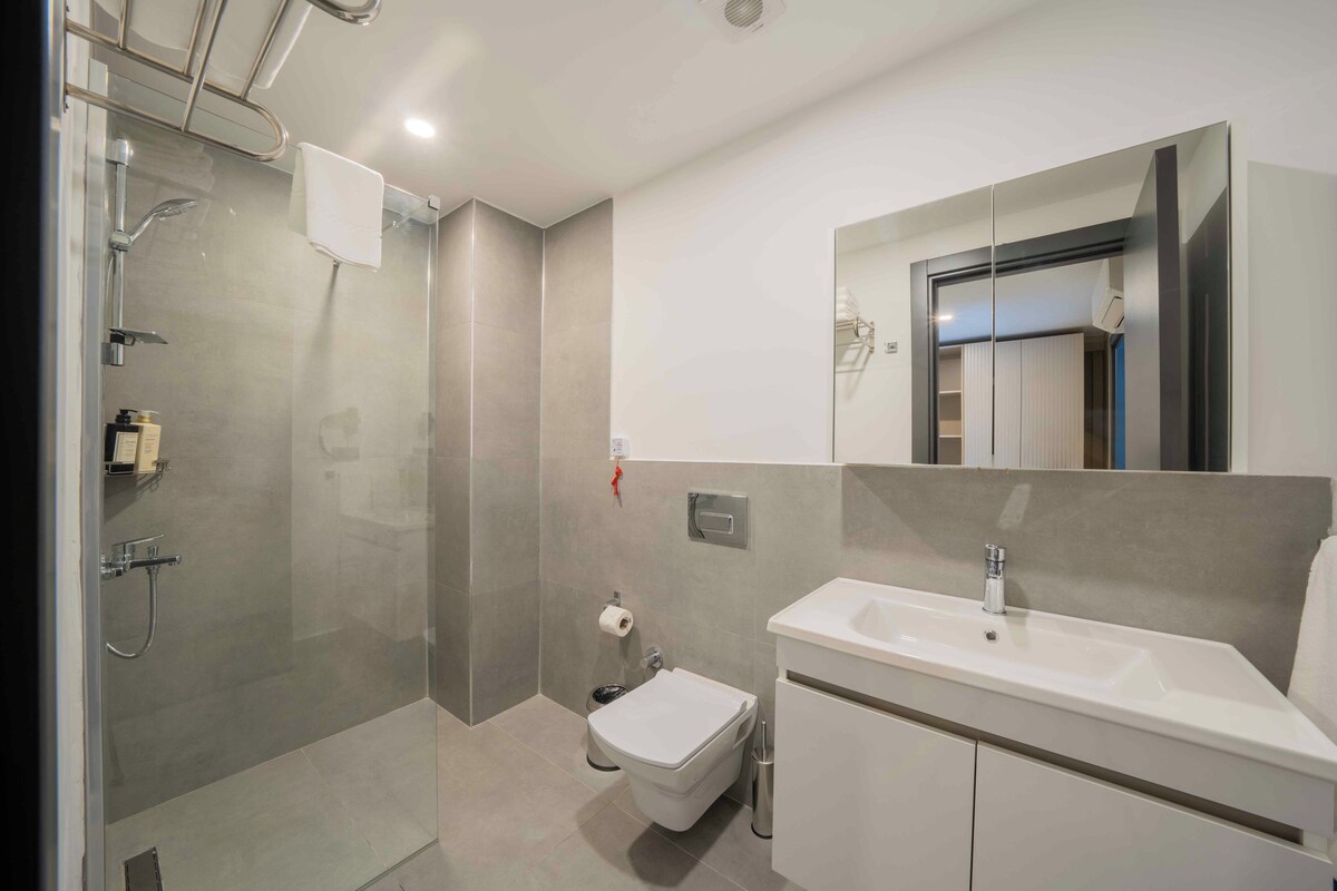 Ein modernes Badezimmer mit einer Duschkabine, einer Toilette und einem Waschbecken mit Spiegel darüber.