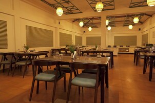 A spacious dining area with multiple tables and chairs, wooden flooring, and pendant lighting.