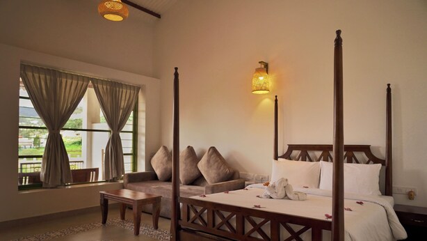 A four-poster bed with a canopy, a sofa, a small table, and a wall-mounted lamp.