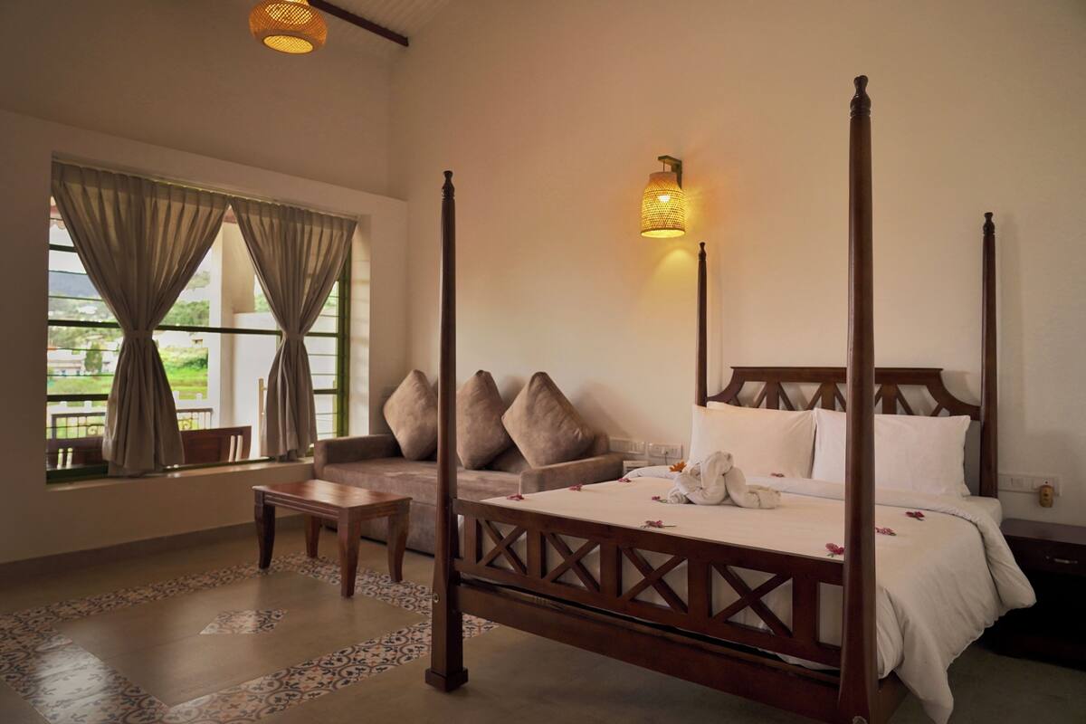 A four-poster bed with a canopy, a sofa, a small table, and a wall-mounted lamp.