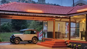 A vintage car parked in front of a building with a red-tiled roof and a glass entrance.