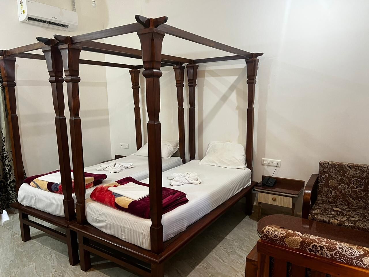 A four-poster canopy bed with white linens and red accents, a small bedside table with a lamp, and a patterned sofa.