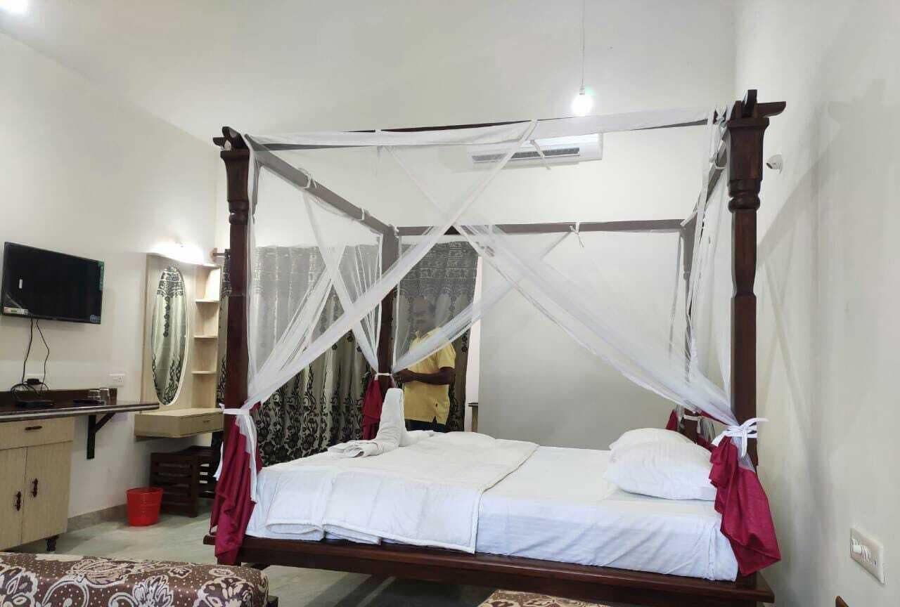A four-poster bed with a canopy, a bedside table, a mirror, and a television on the wall.