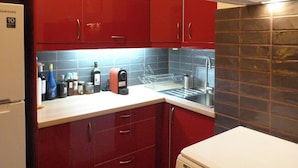Una cocina pequeña con armarios rojos, una encimera blanca y un fregadero de acero inoxidable.