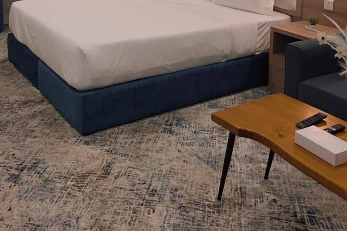 A hotel room with a large bed, bedside tables, a desk, and an air conditioning unit.