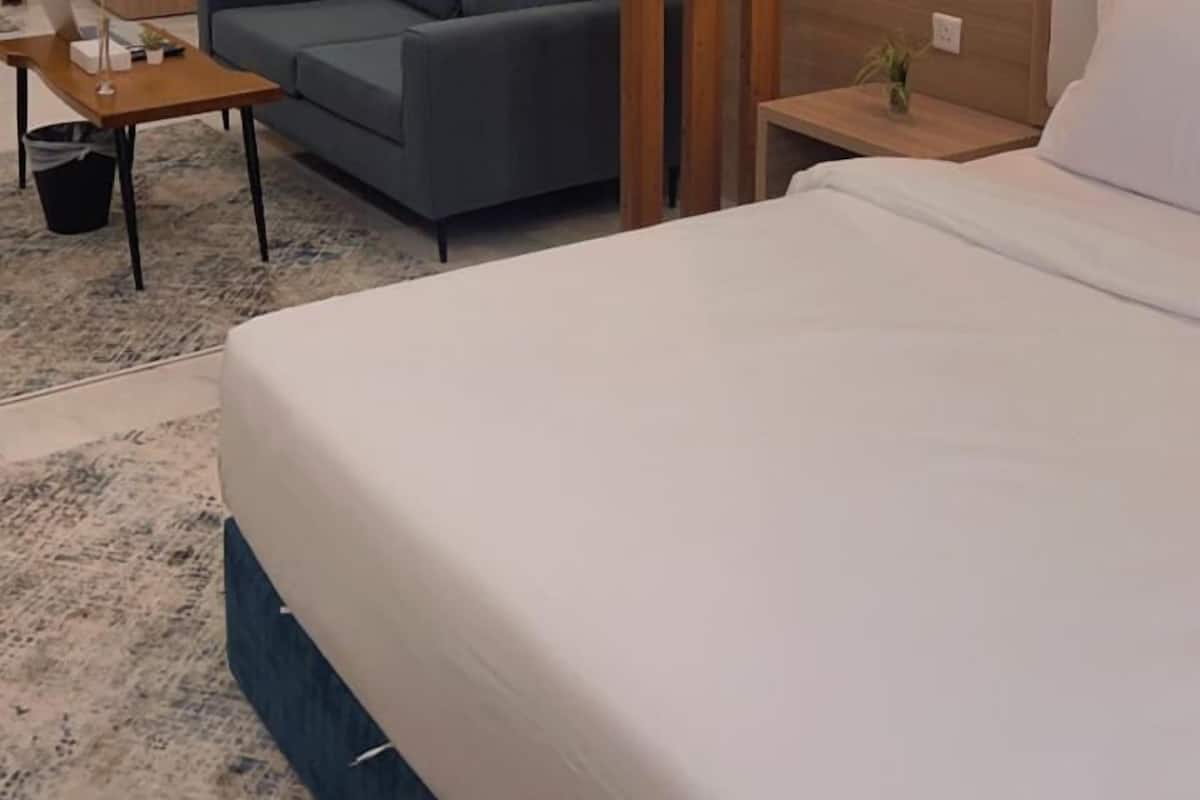 A modern hotel room with a large bed, a sofa, a wooden accent wall, and a nightstand with a lamp.