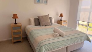 Un dormitorio con una cama, dos mesitas de noche, un ventanal y un cuadro en la pared.