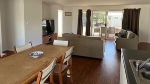 Una sala de estar con televisor, sofá, mesa de comedor, sillas y puerta corrediza de vidrio que da a un área exterior.