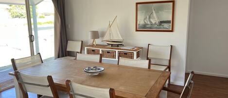 Zona pranzo con tavolo in legno, sei sedie, un modellino di una barca a vela, cesti in vimini e un quadro appeso al muro.