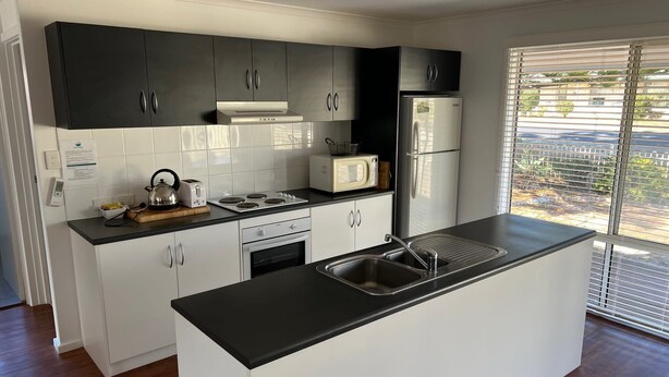 Una cocina moderna con muebles negros y blancos, microondas integrado, refrigerador de acero inoxidable y una isla grande con pileta.
